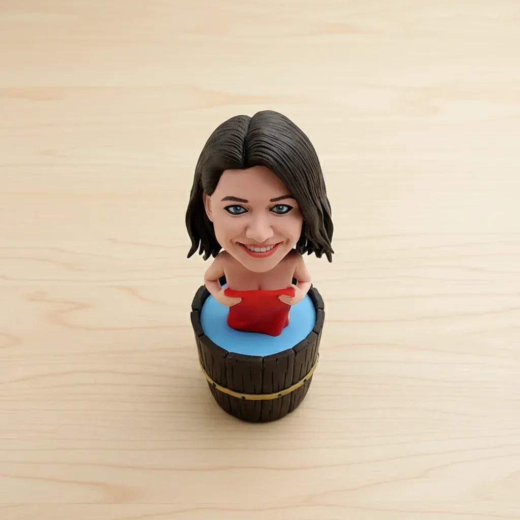 Custom female bobblehead relaxing in a wooden bathtub with a red towel, displayed on a spa-style shelf with rolled towels, soap, and bath salts2ccf1f62e458.webp
