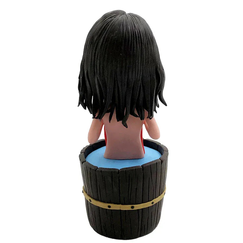 Custom female bobblehead relaxing in a wooden bathtub with a red towel, displayed on a spa-style shelf with rolled towels, soap, and bath salts.webp